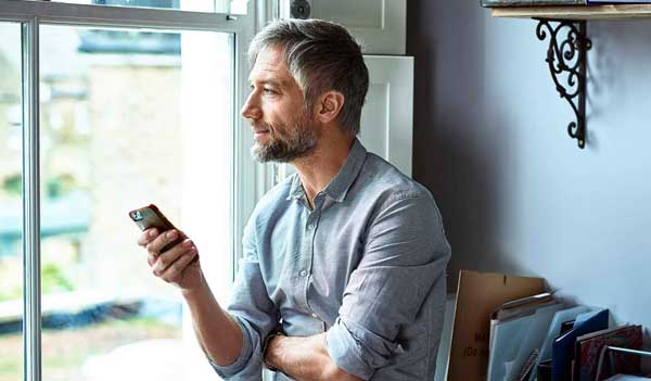 Man holding phone looking out of a window